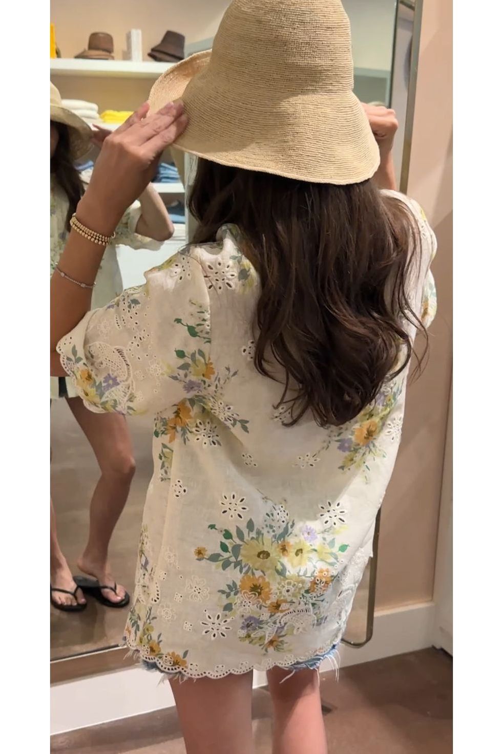 Person wearing a floral dress and straw hat in a mirror reflection.