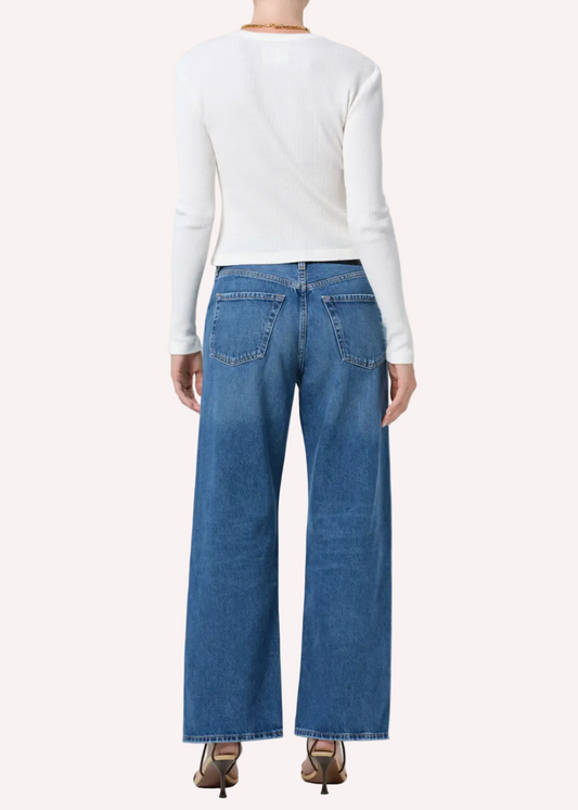 Person wearing a white long-sleeve shirt and blue jeans on a plain background