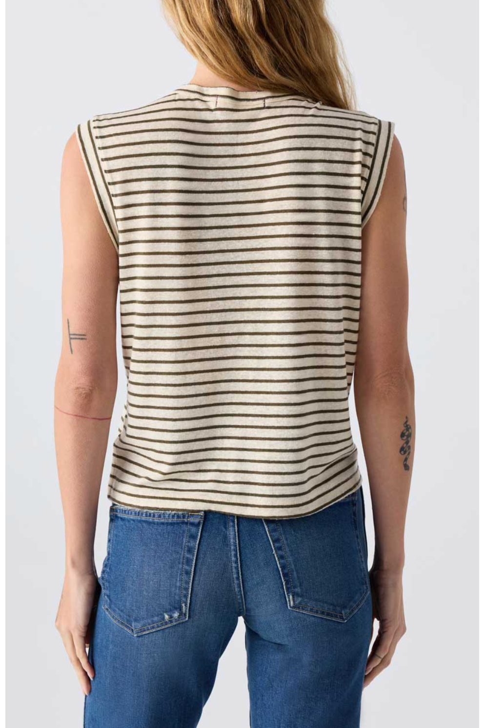 Person wearing a striped sleeveless top and blue jeans on a plain background