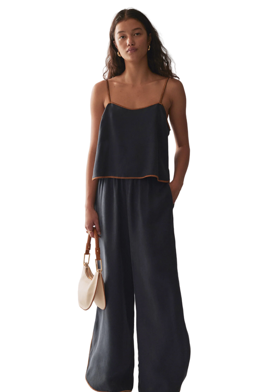 Woman wearing a black sleeveless top and wide-leg pants against a marble wall.