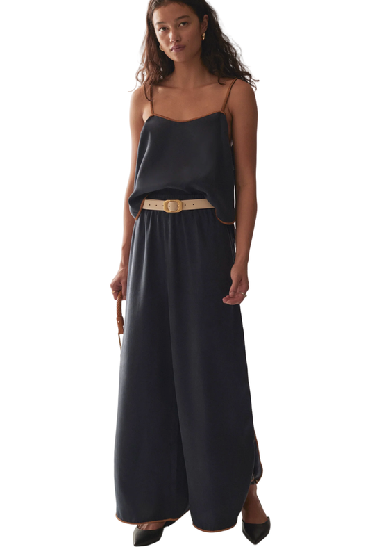 Woman wearing a black slip dress with a beige belt on a marble background