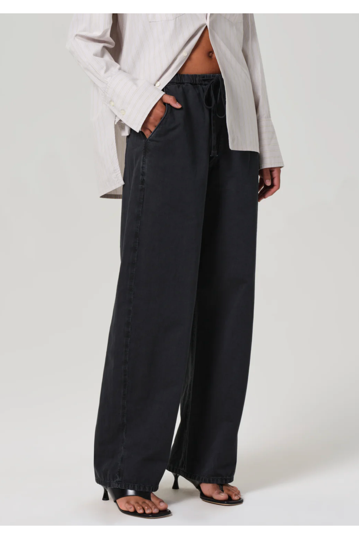 Person wearing black wide-leg pants with a light gray top on a white background