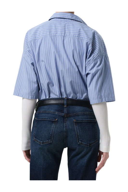 Person wearing a blue striped shirt and dark jeans from behind on a plain background