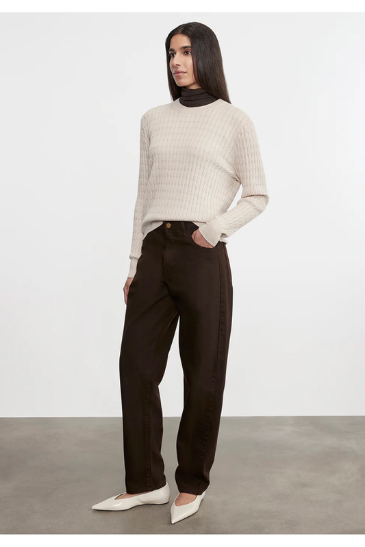 Woman wearing a beige sweater and black pants against a white background