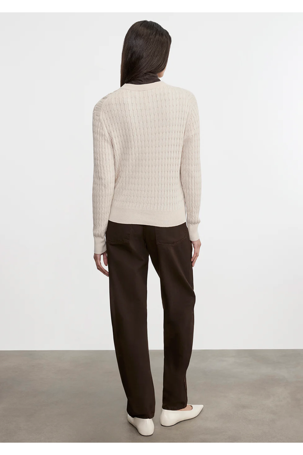 Person wearing a white ribbed sweater and dark pants against a plain background
