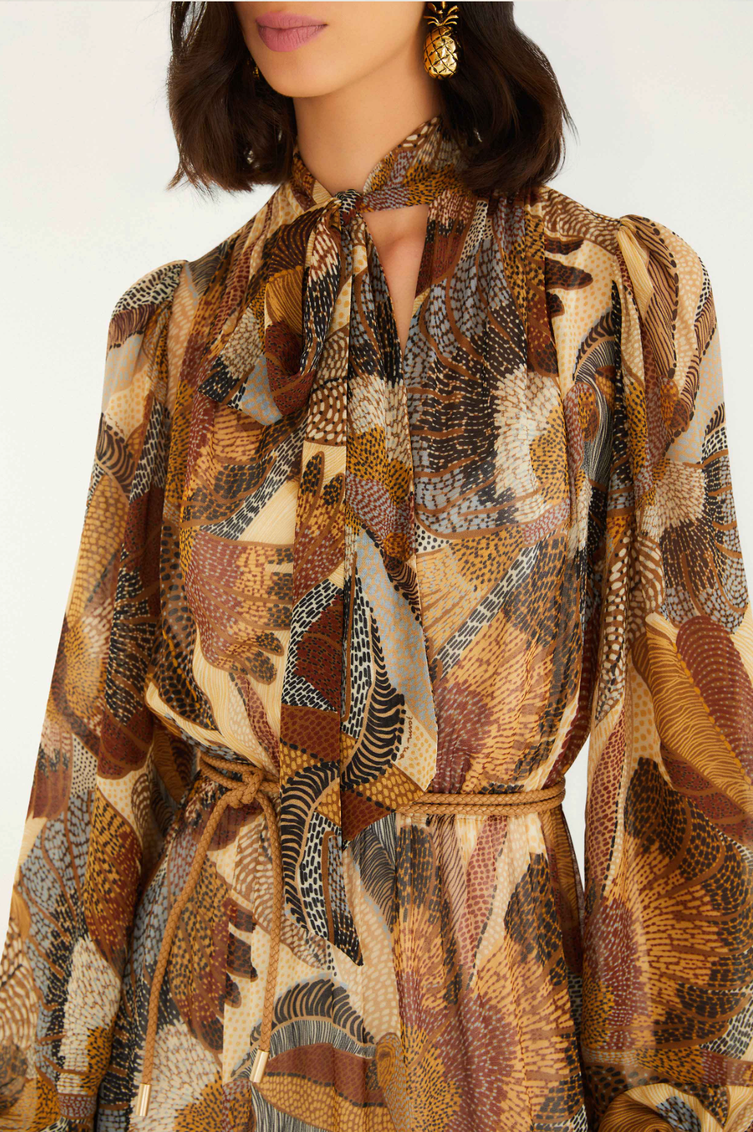 Woman wearing a patterned dress with a scarf around her neck against a white background