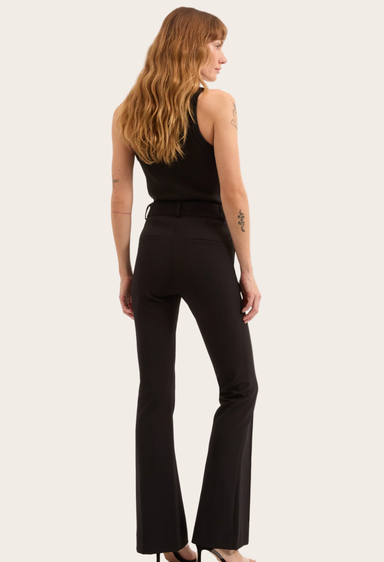 Woman wearing black flared pants and a black top on a white background