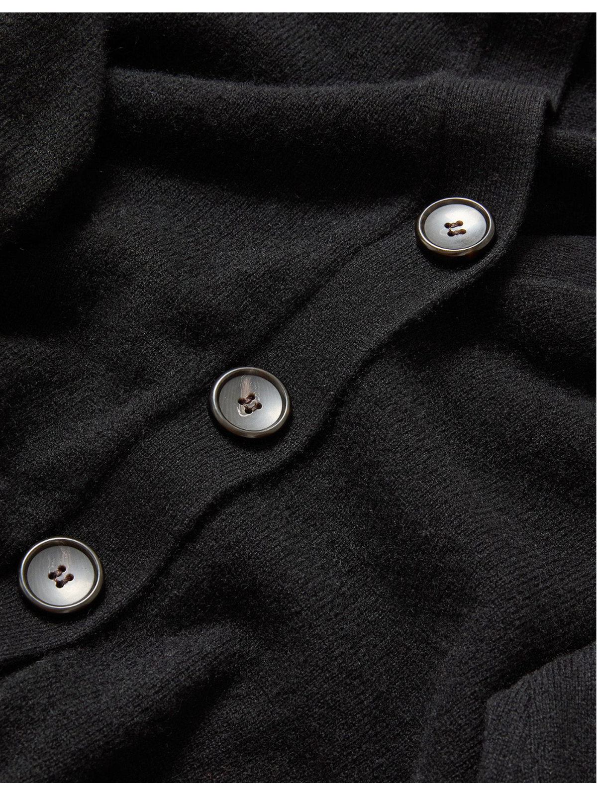 Close-up of a black garment with buttons on a dark background