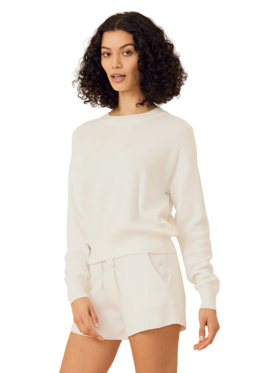 Woman wearing a white sweater and shorts on a beige background