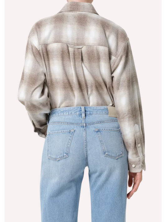 Person wearing a patterned shirt and light blue jeans on a white background