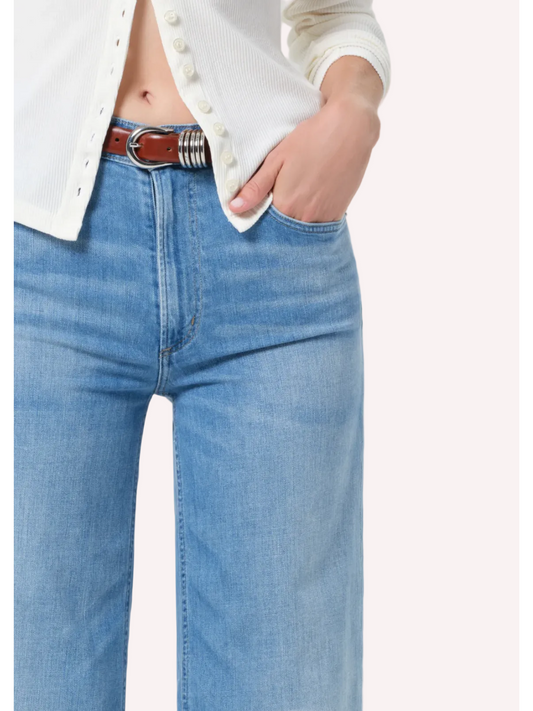 Person wearing blue jeans with a white shirt on a plain background