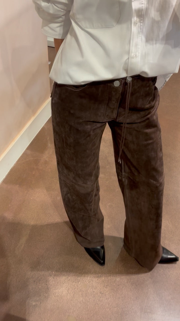 Person wearing brown pants and a light-colored shirt on a neutral background