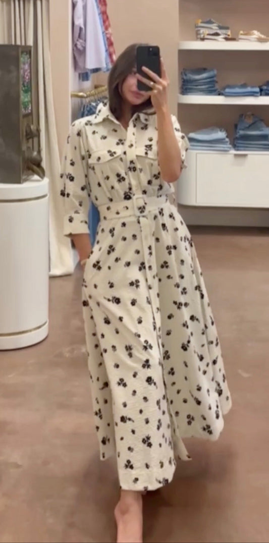 Woman taking a mirror selfie wearing a white dress with black patterns in a store setting.