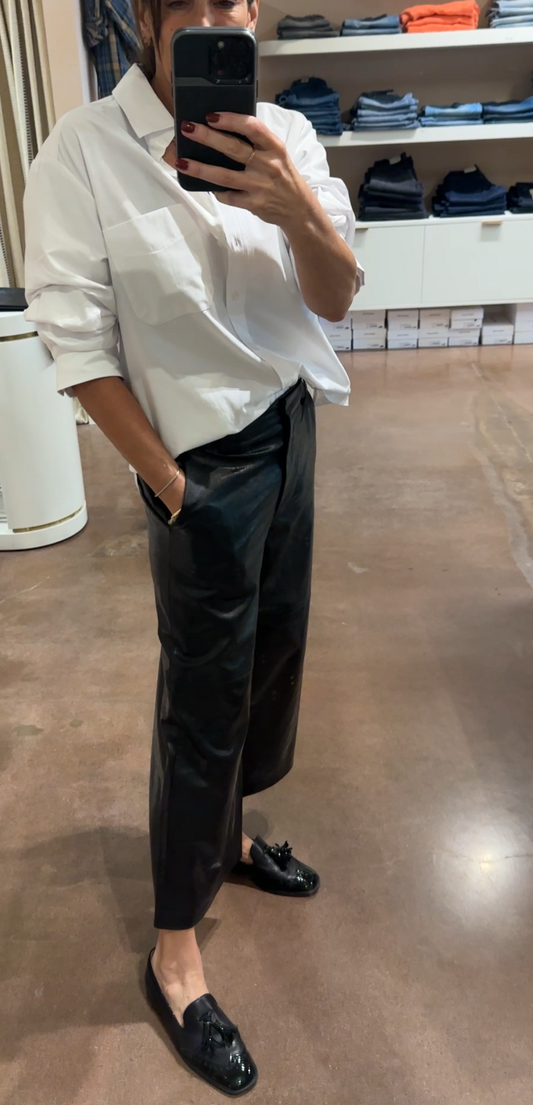 Person taking a mirror selfie wearing a white shirt and black pants in a store setting.