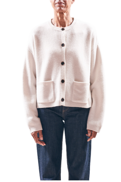 Person wearing a cream cardigan with black buttons on a light pink background