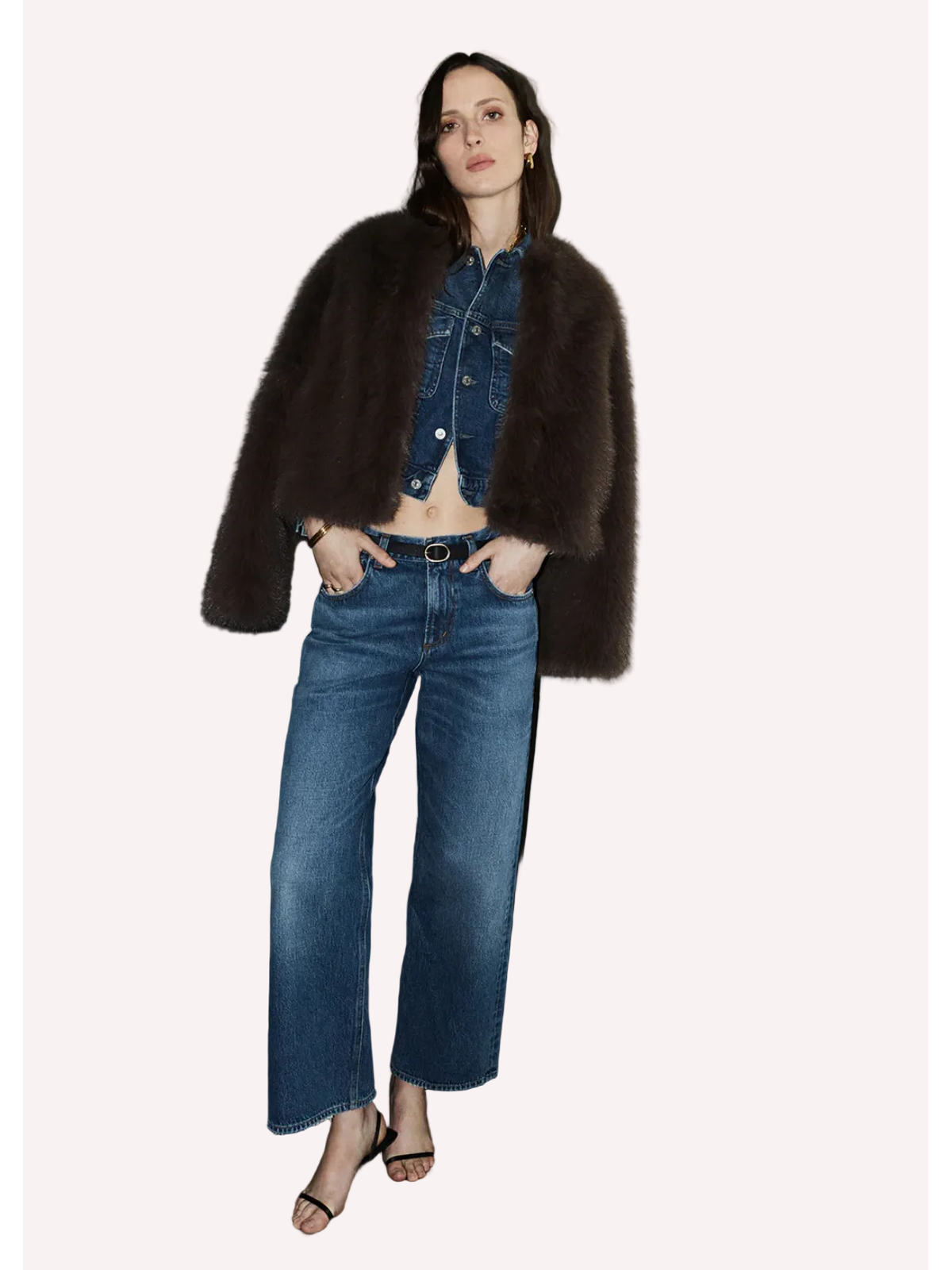 Woman wearing a dark fur coat, denim jacket, and jeans standing on a staircase.
