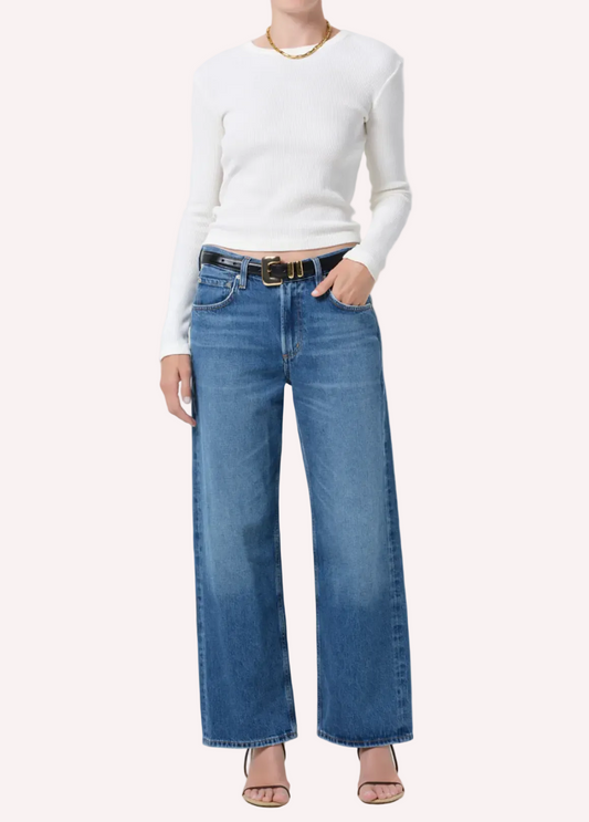 Person wearing a white long-sleeve top and blue jeans on a white background