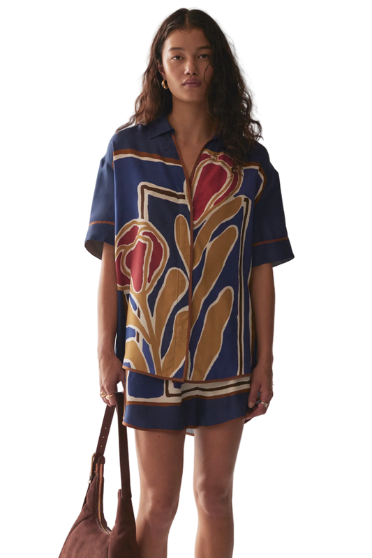 Woman wearing a patterned shirt and shorts set with a marble background