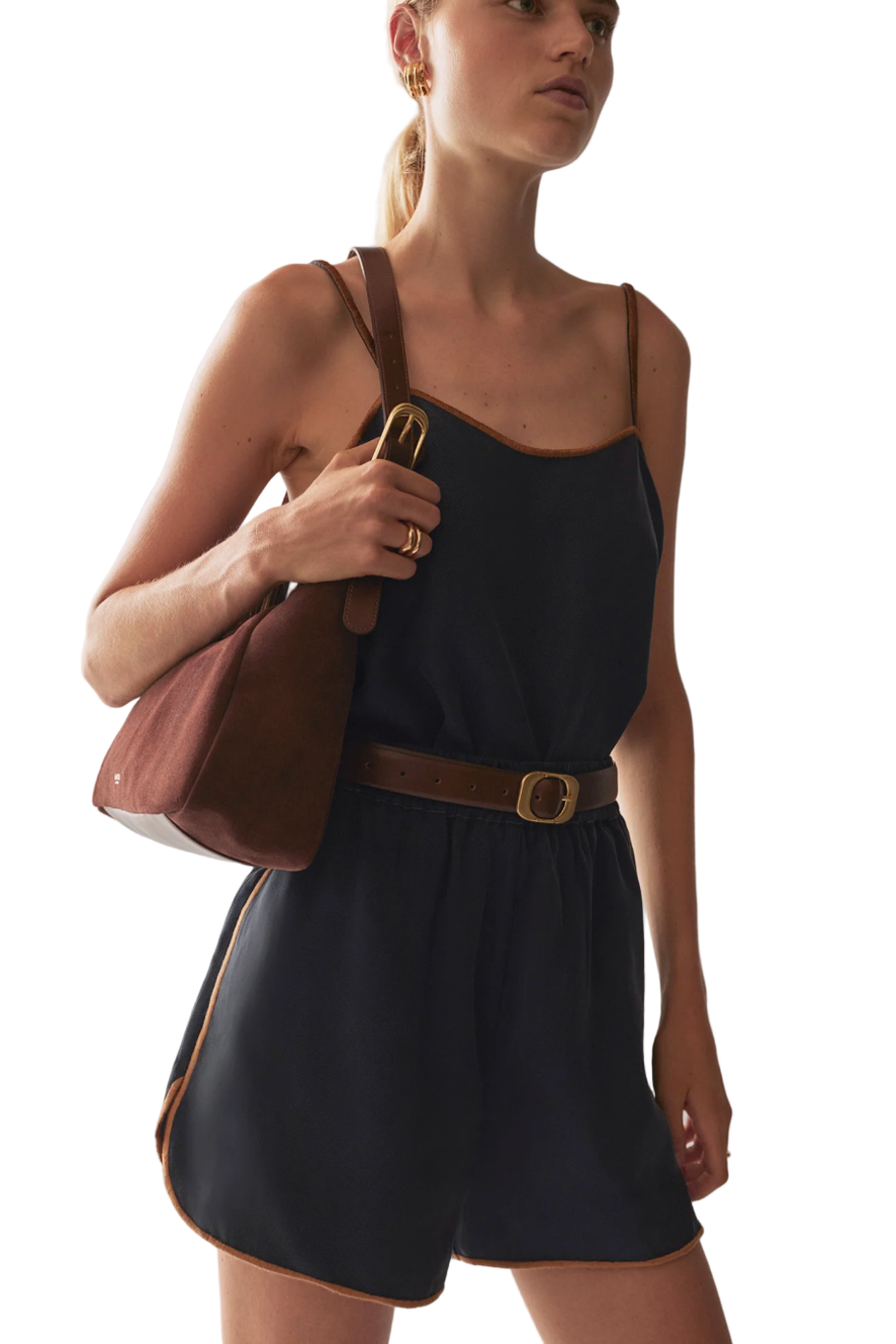 Woman wearing a navy shorts with a brown belt and carrying a brown handbag on a white background