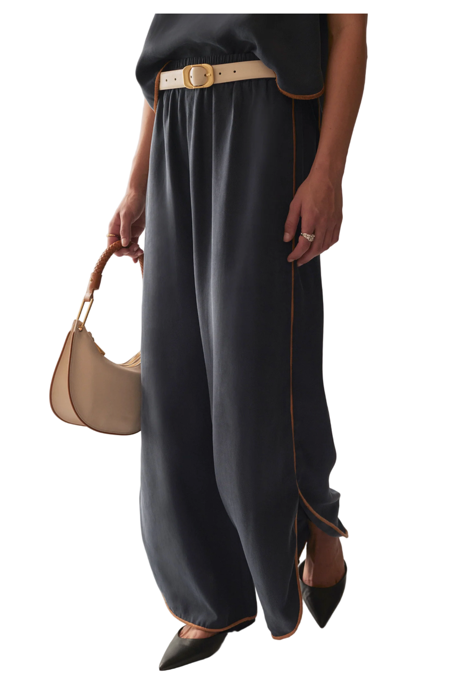 Person wearing navy pants with a beige belt and holding a beige handbag on a marble floor.