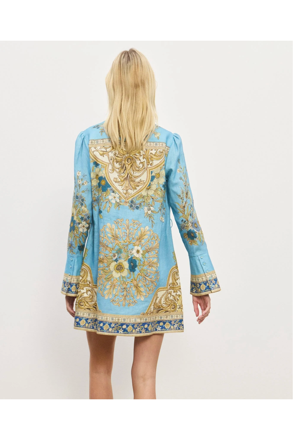 Woman wearing a blue dress with gold and white floral patterns on a white background