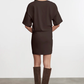 Woman wearing a brown outfit with knee-high boots on a plain background