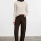 Woman wearing a beige sweater and dark pants against a white background