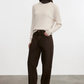Woman wearing a beige sweater and black pants against a white background