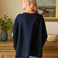 Person wearing a navy sweater in a room with a painting and decorative items.
