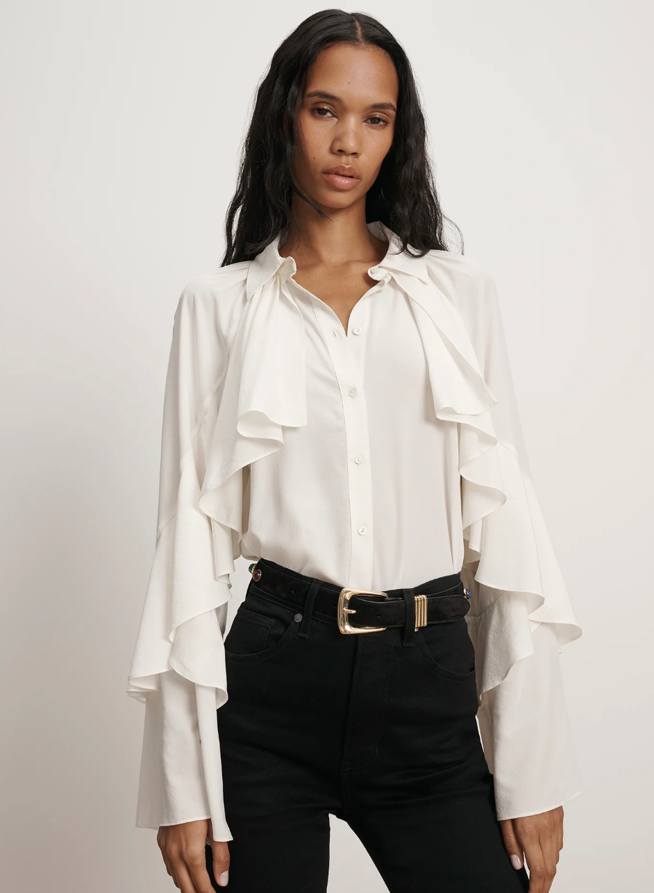 Woman wearing a white blouse with ruffled sleeves and black pants on a plain background