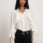 Woman wearing a white blouse with ruffled sleeves and black pants on a plain background