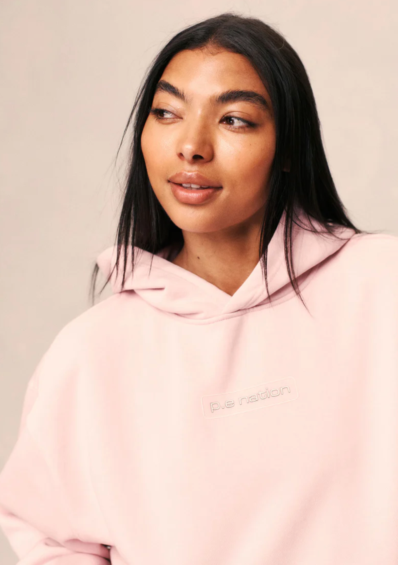 Woman wearing a pink hoodie with a brand logo on a plain background