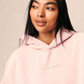 Woman wearing a pink hoodie with a brand logo on a plain background