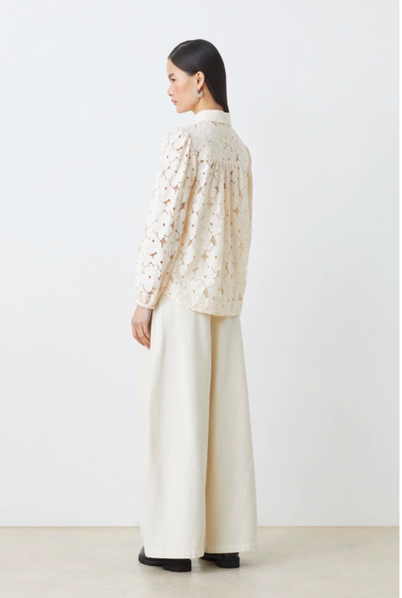 Woman wearing a cream-colored blouse with a textured pattern and wide-leg pants on a white background