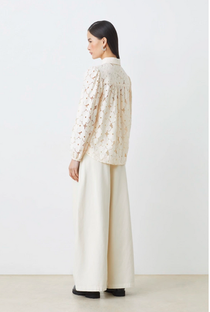 Woman wearing a cream-colored blouse with a textured pattern and wide-leg pants on a white background