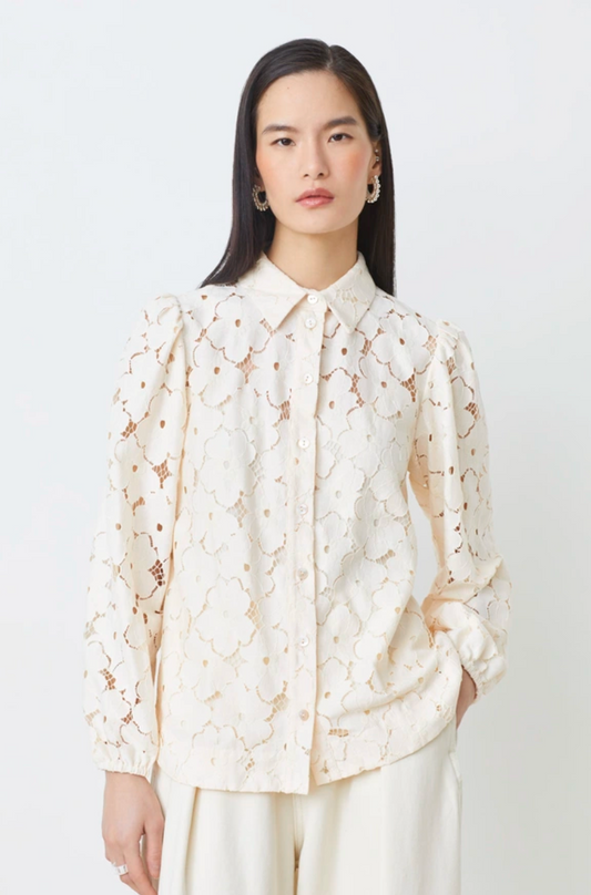 Woman wearing a cream-colored lace blouse against a white background