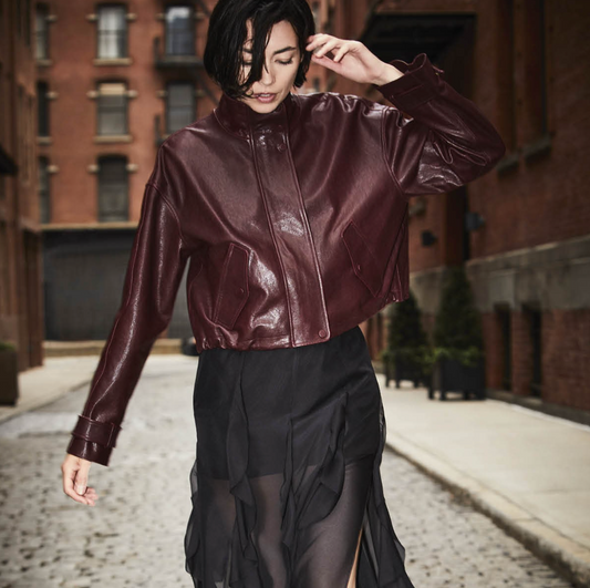Person wearing a shiny burgundy jacket and black skirt on a street with brick buildings.