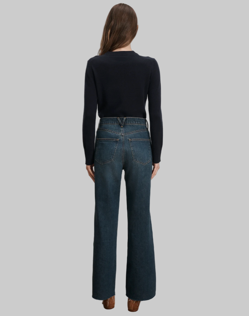 Person wearing blue jeans and a black top standing against a plain background