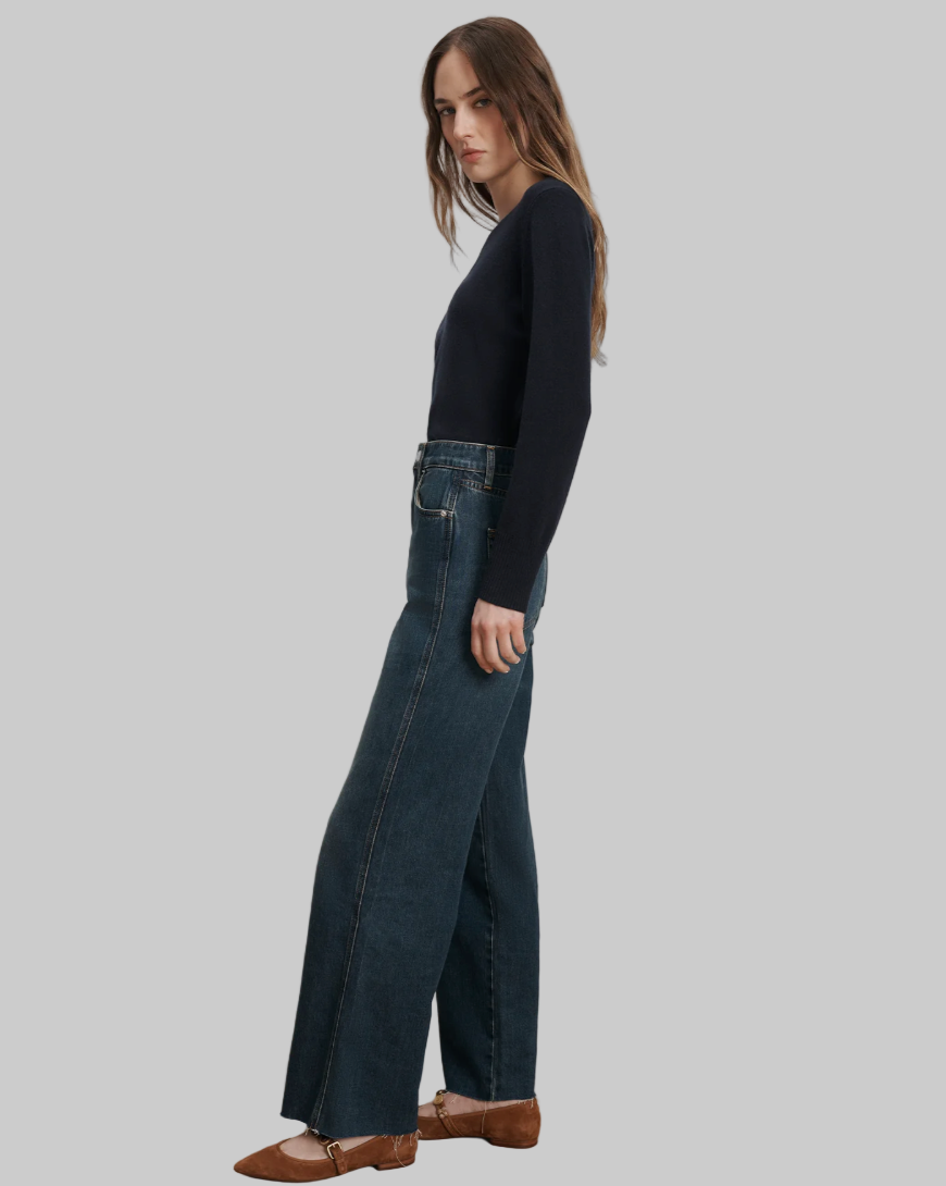 Woman wearing dark blue jeans and a black top against a plain background