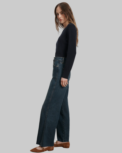 Woman wearing dark blue jeans and a black top against a plain background