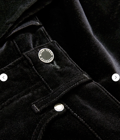 Woman wearing a sleeveless patterned top and black flared pants on a plain background