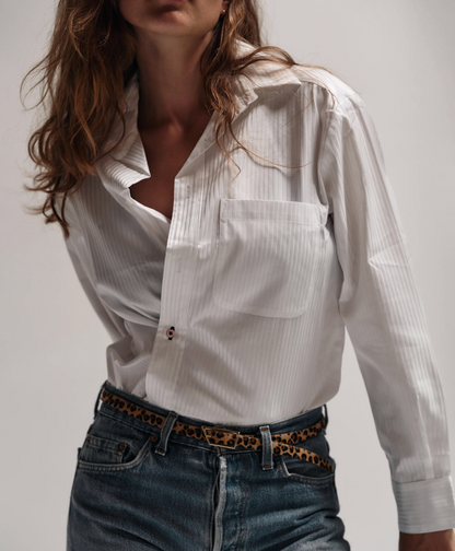 Person wearing a white striped shirt and blue jeans with a leopard print belt on a plain background
