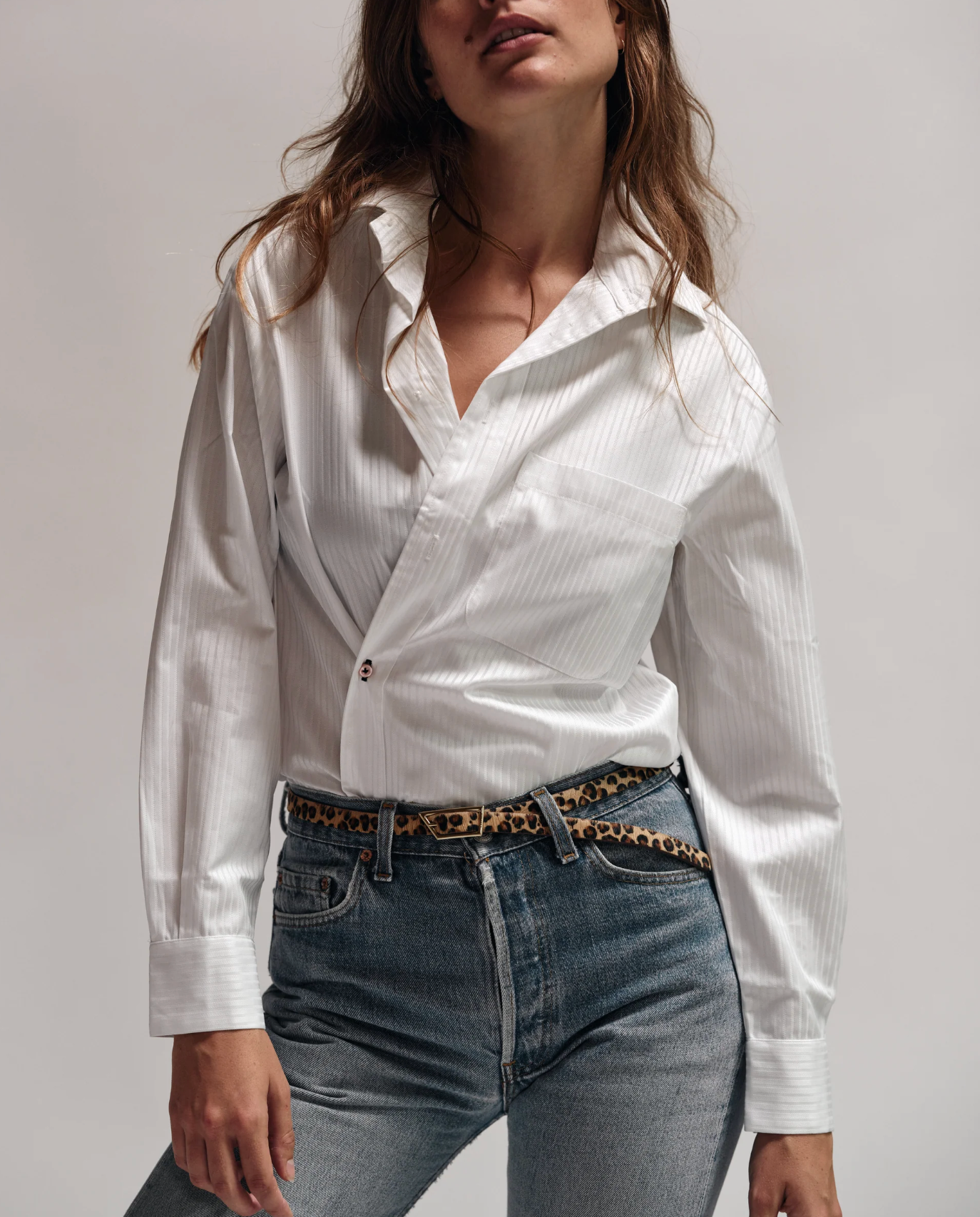 Woman wearing a white shirt and jeans with a leopard print belt against a plain background