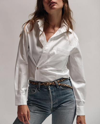 Woman wearing a white shirt and jeans with a leopard print belt against a plain background