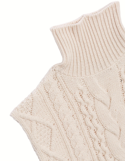 Close-up of a cream-colored knitted sleeveless sweater with cable knit pattern on a light gray background.