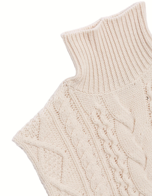 Close-up of a cream-colored knitted sleeveless sweater with cable knit pattern on a light gray background.