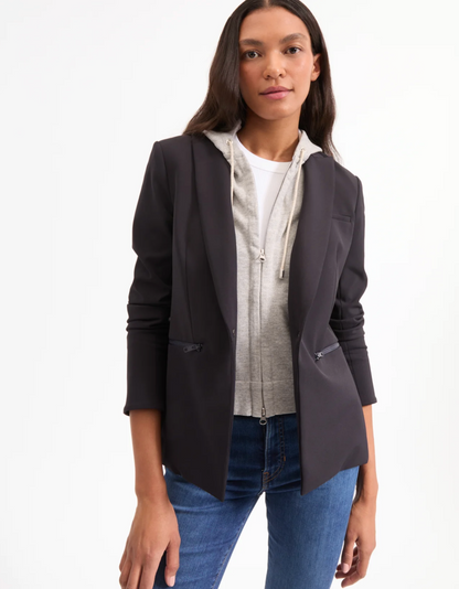 Woman wearing a black blazer over a white shirt with a patterned scarf, standing against a white background.