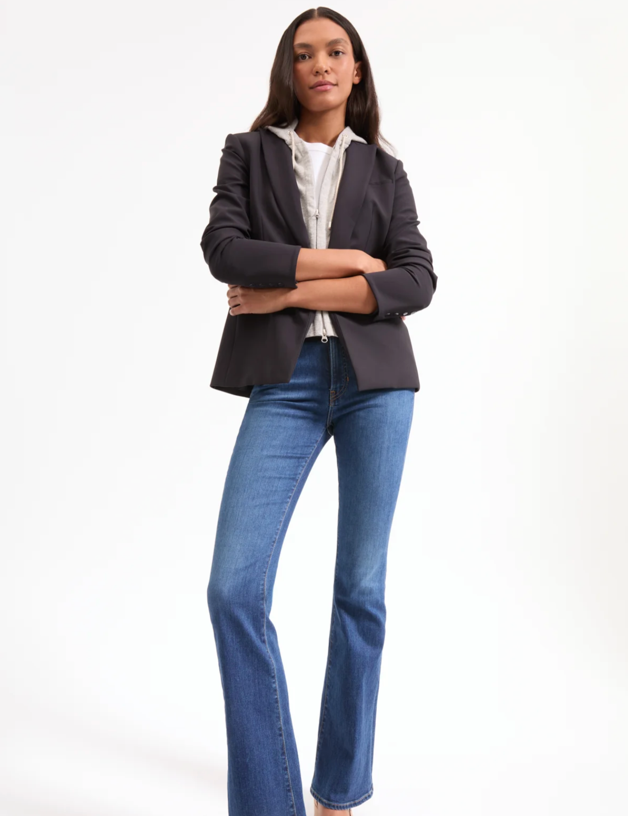 Woman wearing a dark blazer and blue jeans on a white background