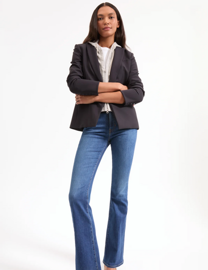 Woman wearing a dark blazer and blue jeans on a white background
