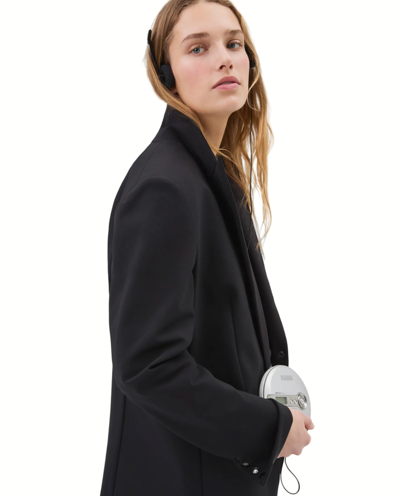 Woman wearing a black coat holding a white device on a plain background